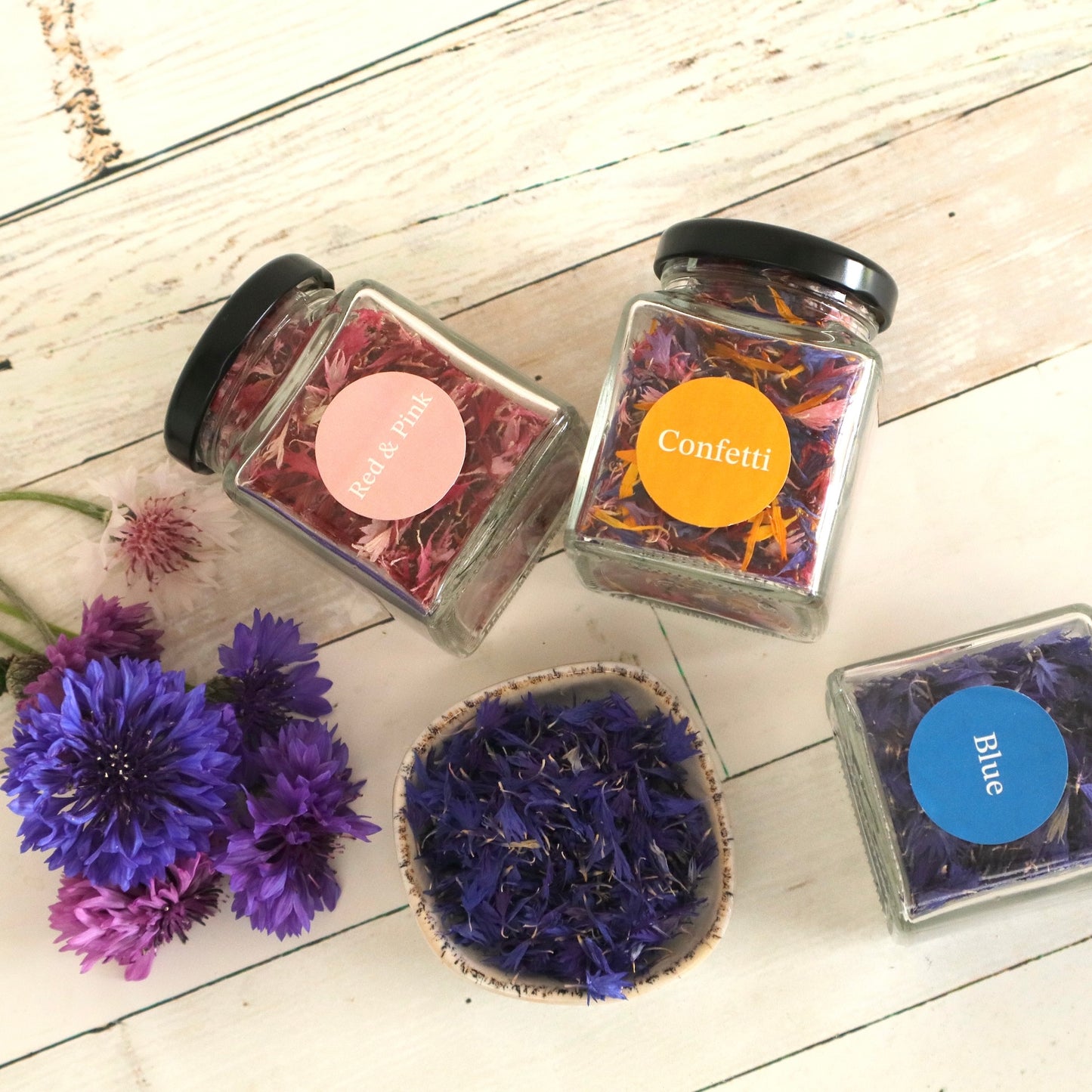 Jars of Native Tree Farm's dried edible flowers with colourful labels on a wooden surface