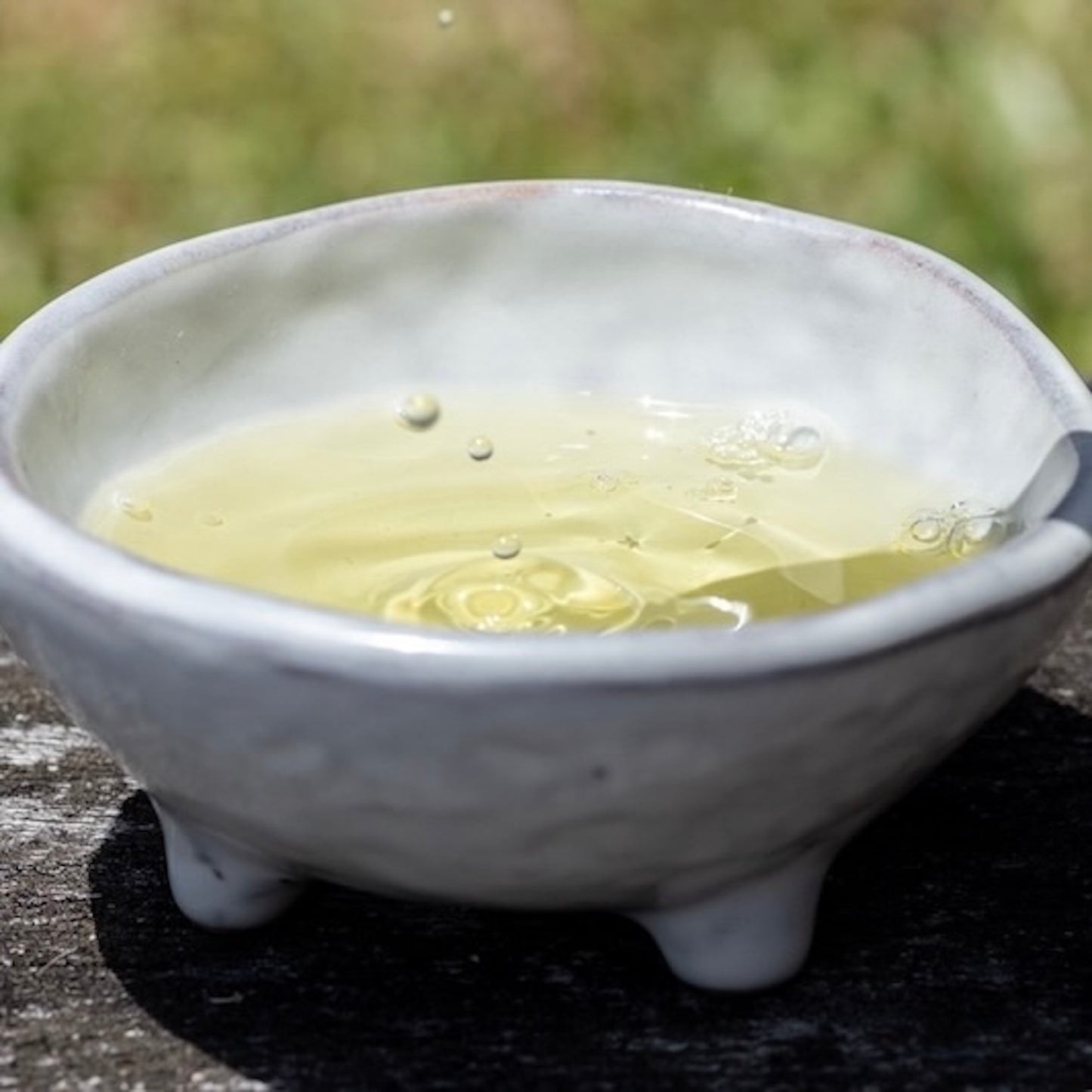 Ceramic bowl with light green kanuka essential oil inside on a dark surface