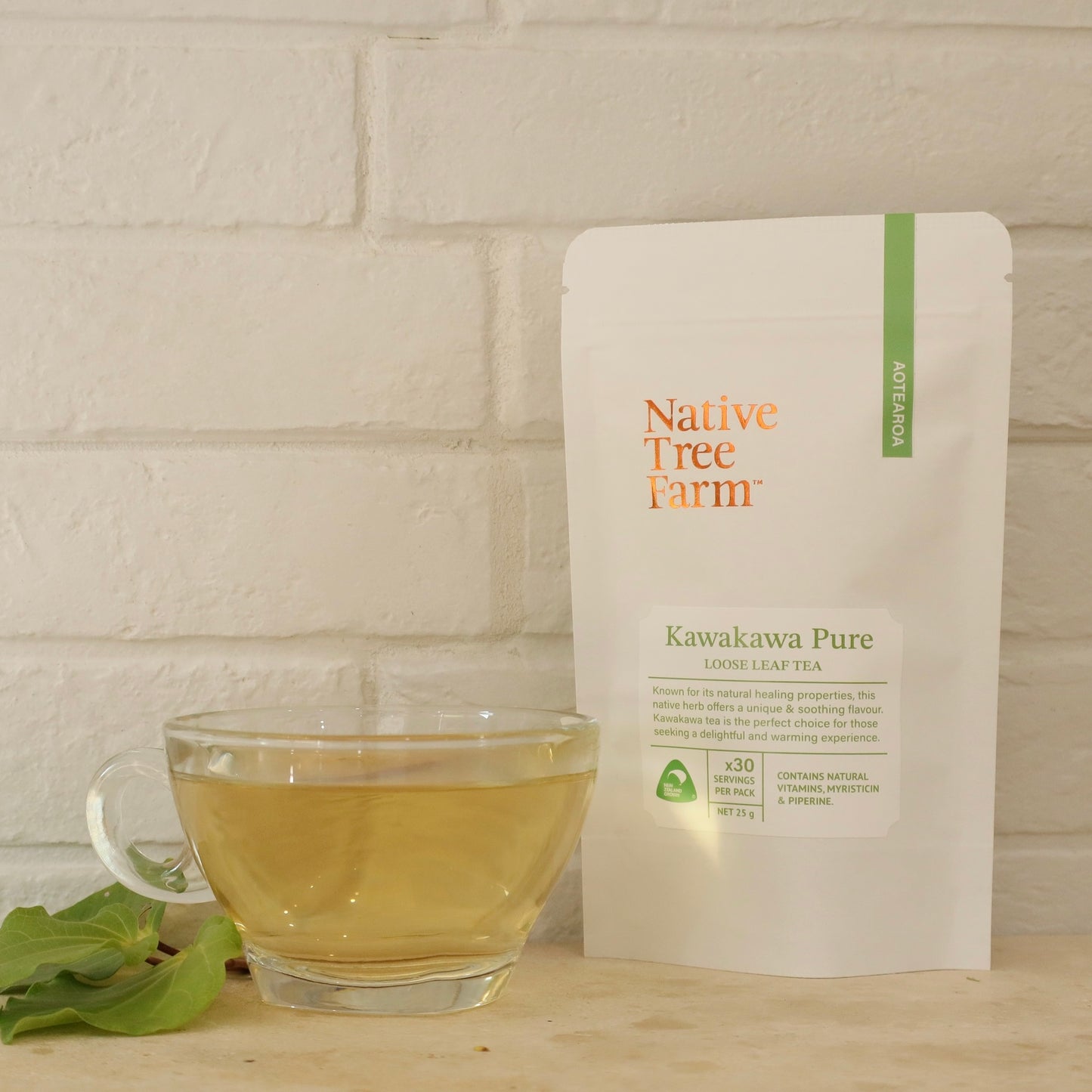Glass cup of kawakawa tea with a package of Native Tree Farm Kawakawa Pure tea on a wooden surface.