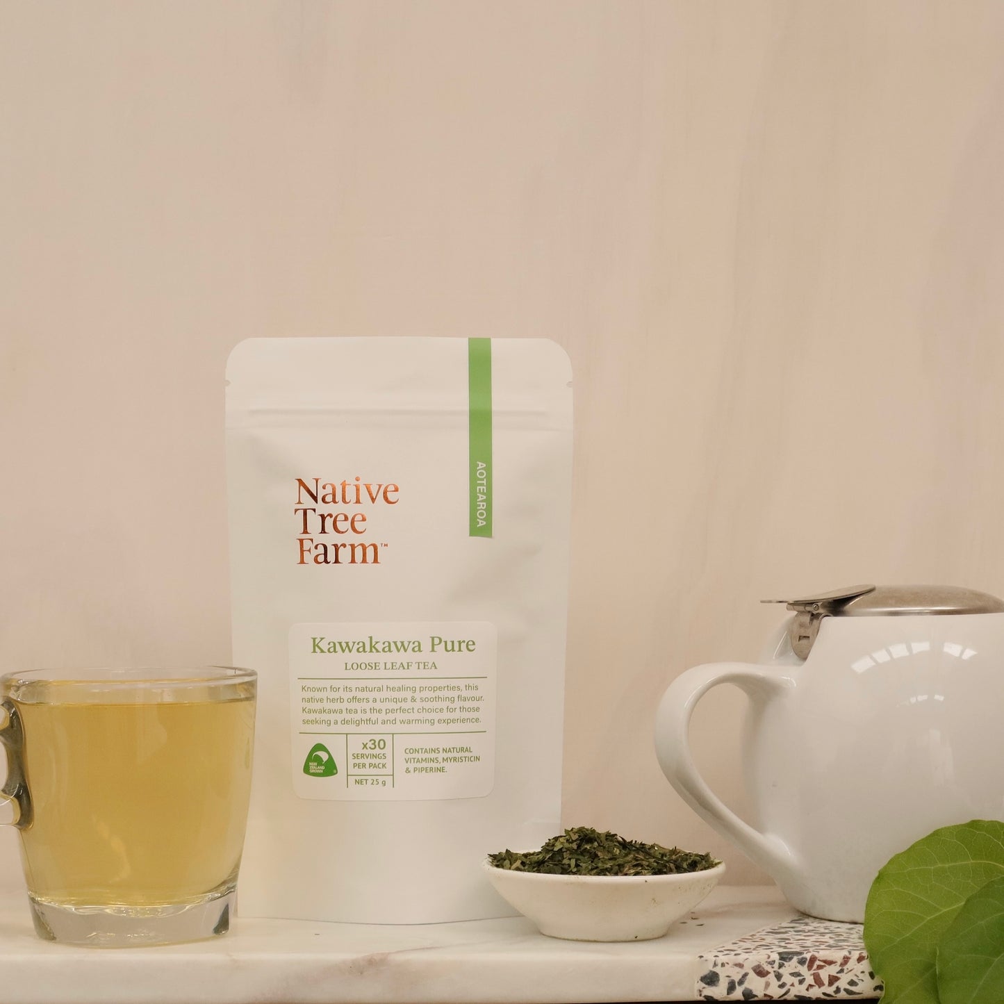 A packaged loose leaf tea product from Native Tree Farm, with a cup of brewed tea and a teapot in the background, set on a white surface.