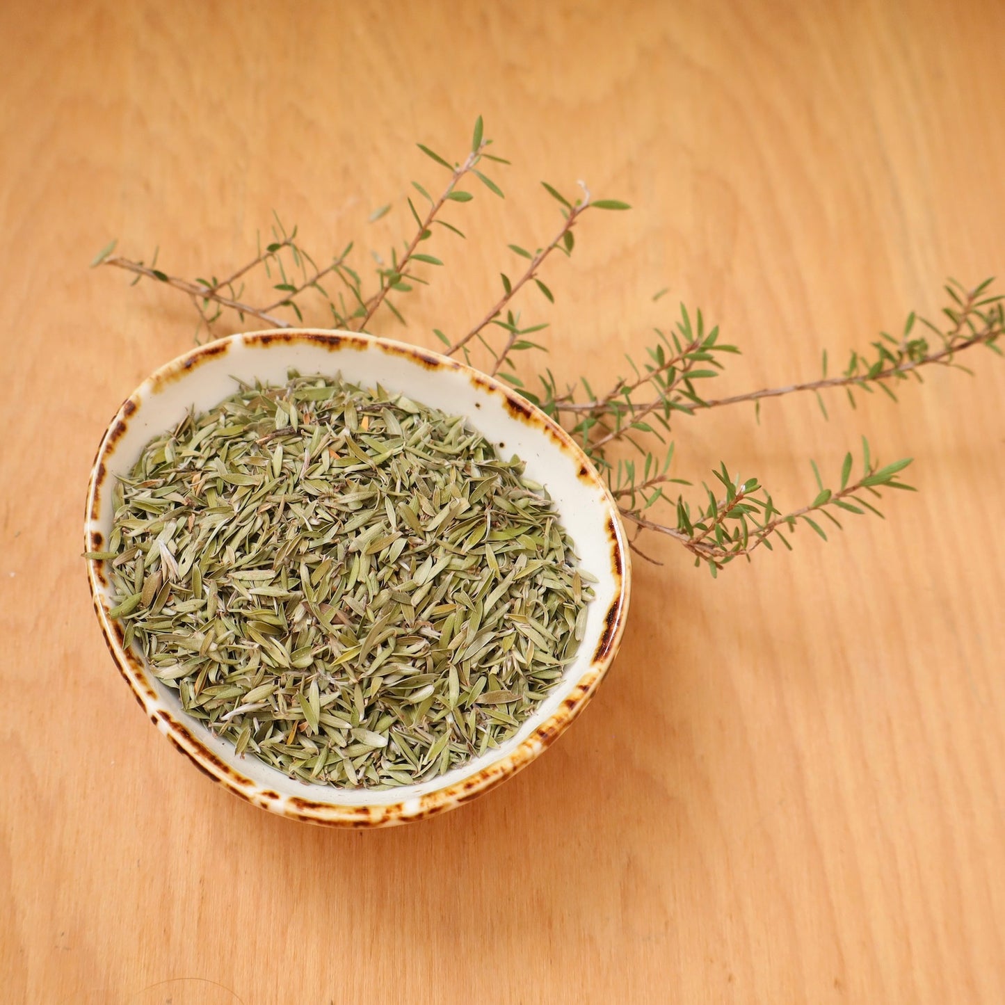 Dried manuka leaf in a ceramic bowl on a wooden surface