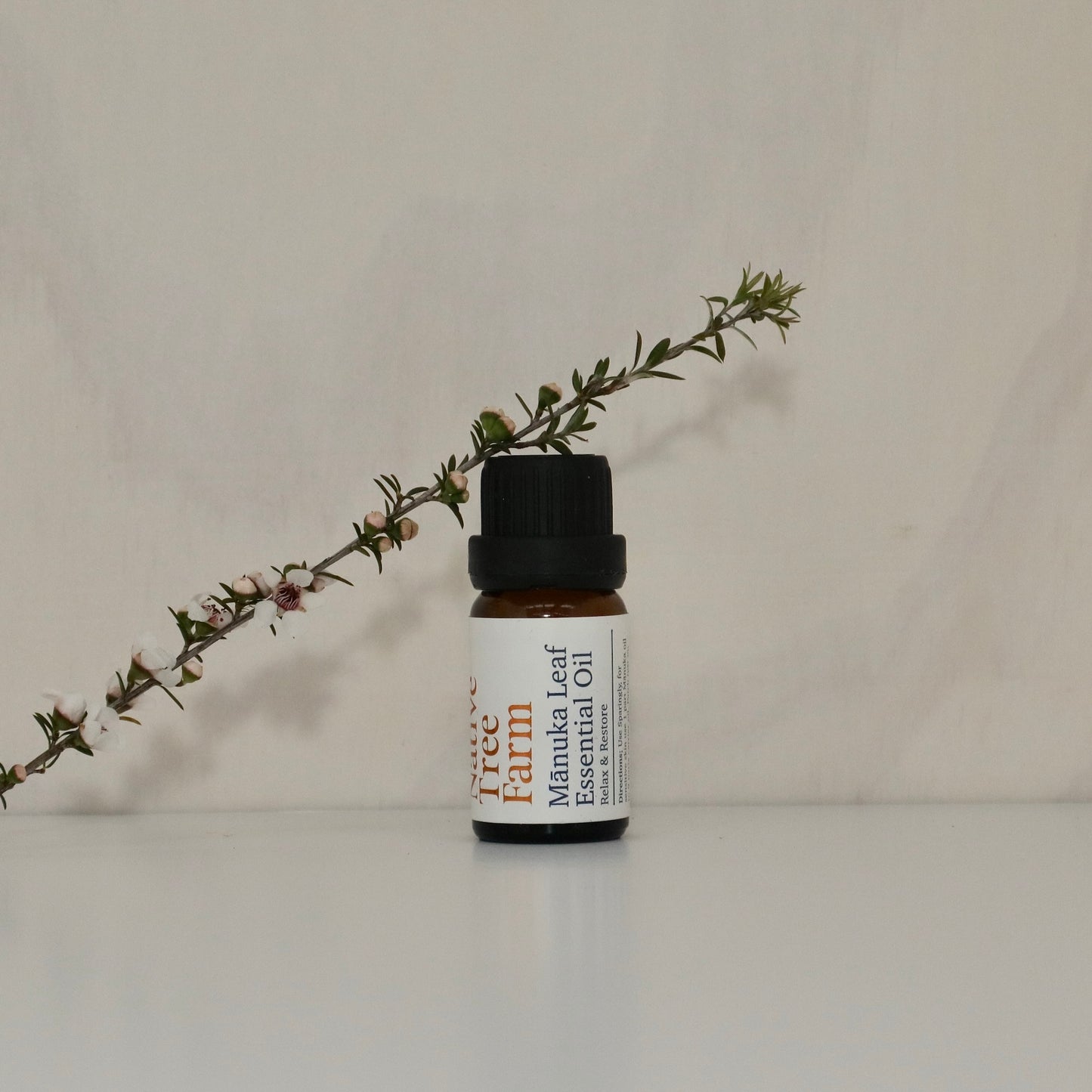 Bottle of Native Tree Farm Manuka Leaf Essential Oil with a manuka branch on a neutral background