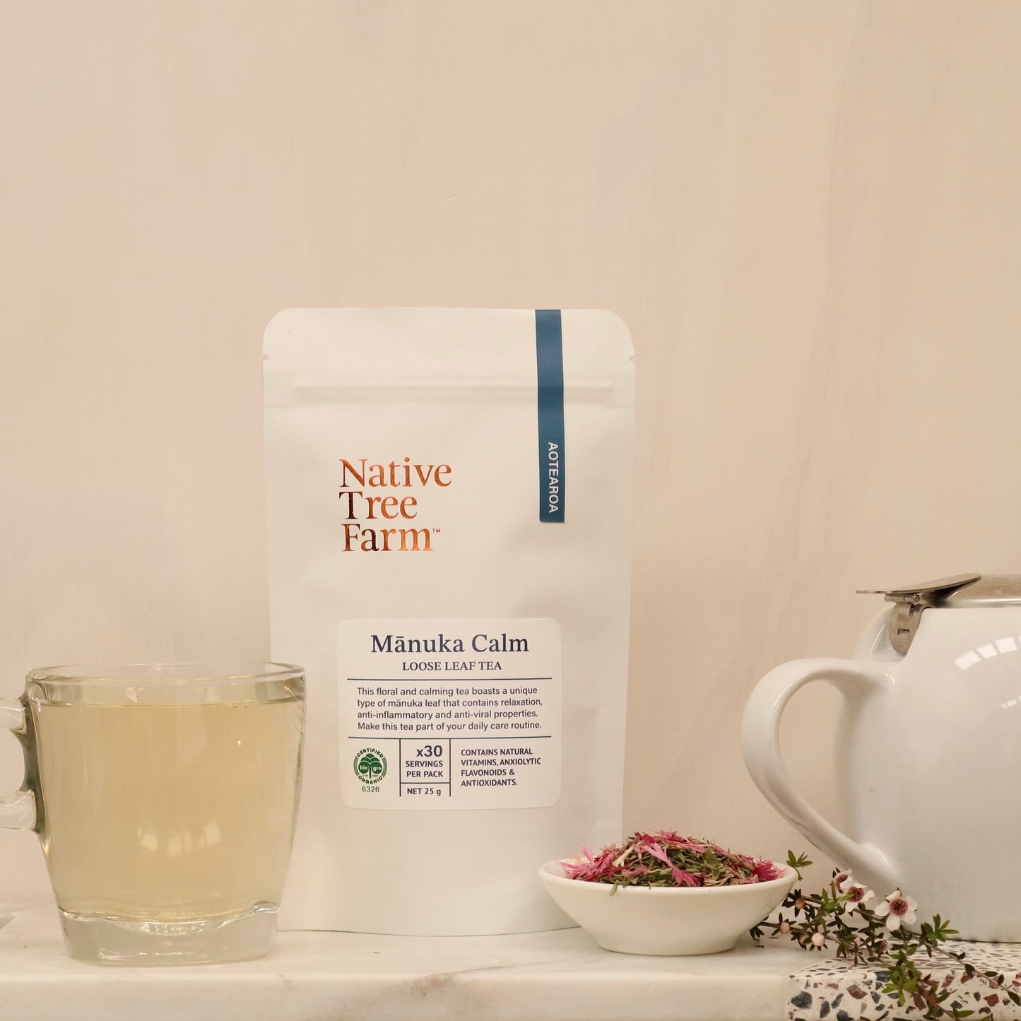 Packaging of Native Tree Farm Manuka Calm loose leaf tea with a cup of brewed tea and a teapot in the background.