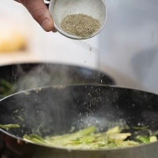native flaky salt seasoning being sprinkled on vegetables in a hot pan.