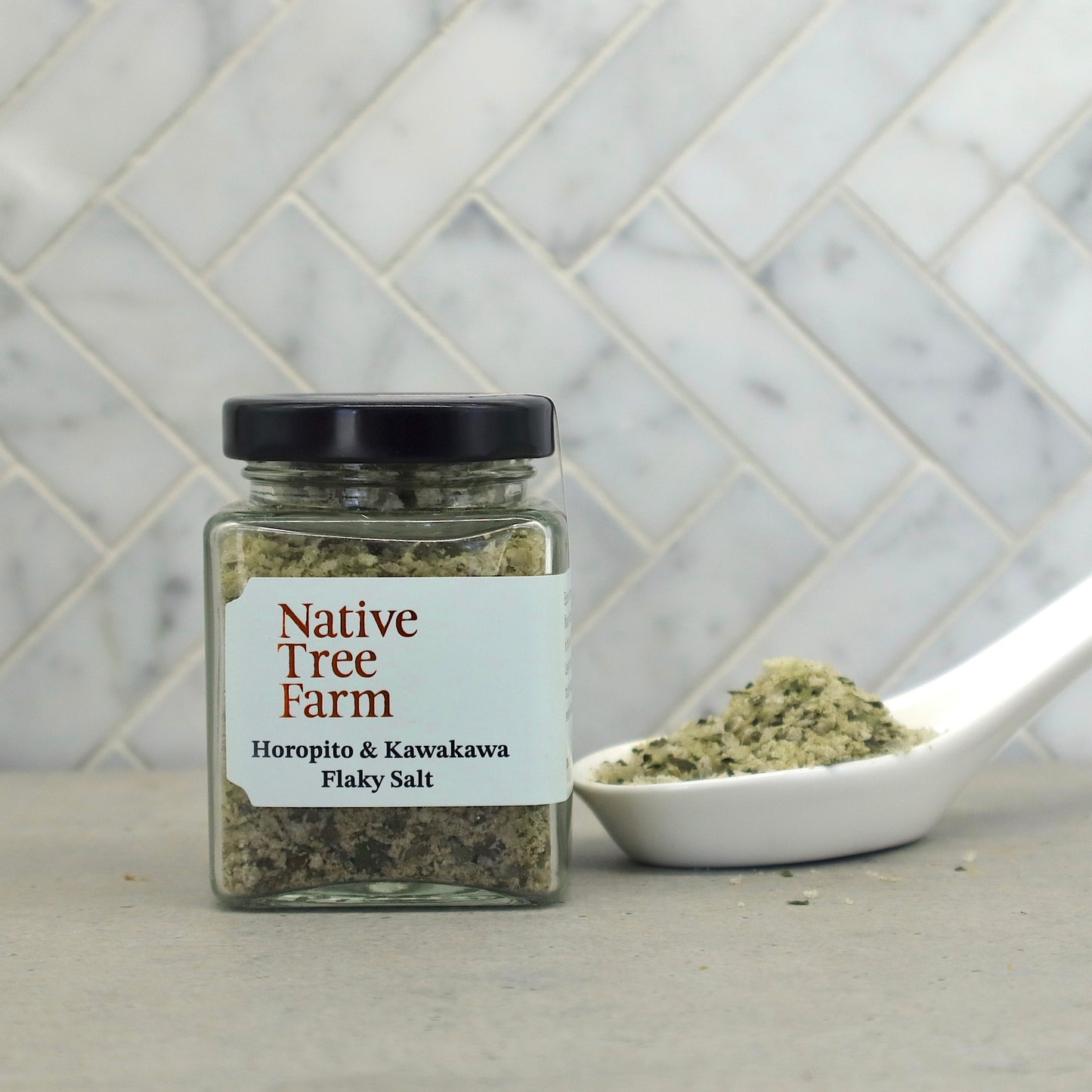Jar of Native Tree Farm Horopito & Kawakawa Flaky Salt with a spoonful of flaky salt on a stone table