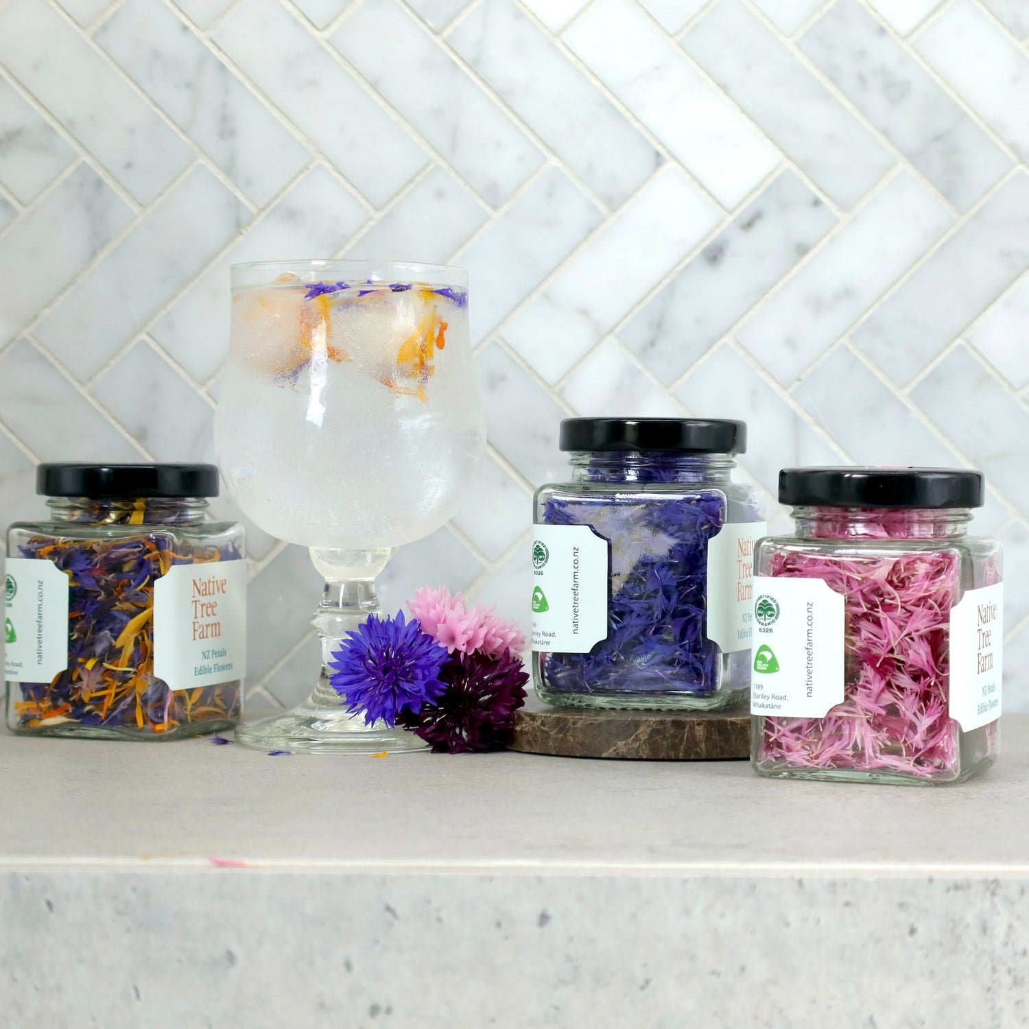 Jars of native tree farms dried edible  flowers next to a cup of fizzy drink