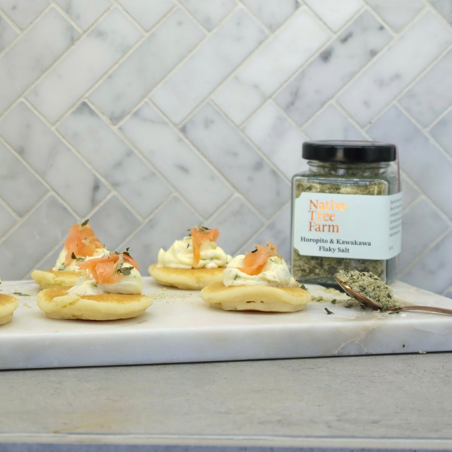 Native Tree Farm's horopito and kawakawa finishing salt on a marble chopping board next to salmon pikelets