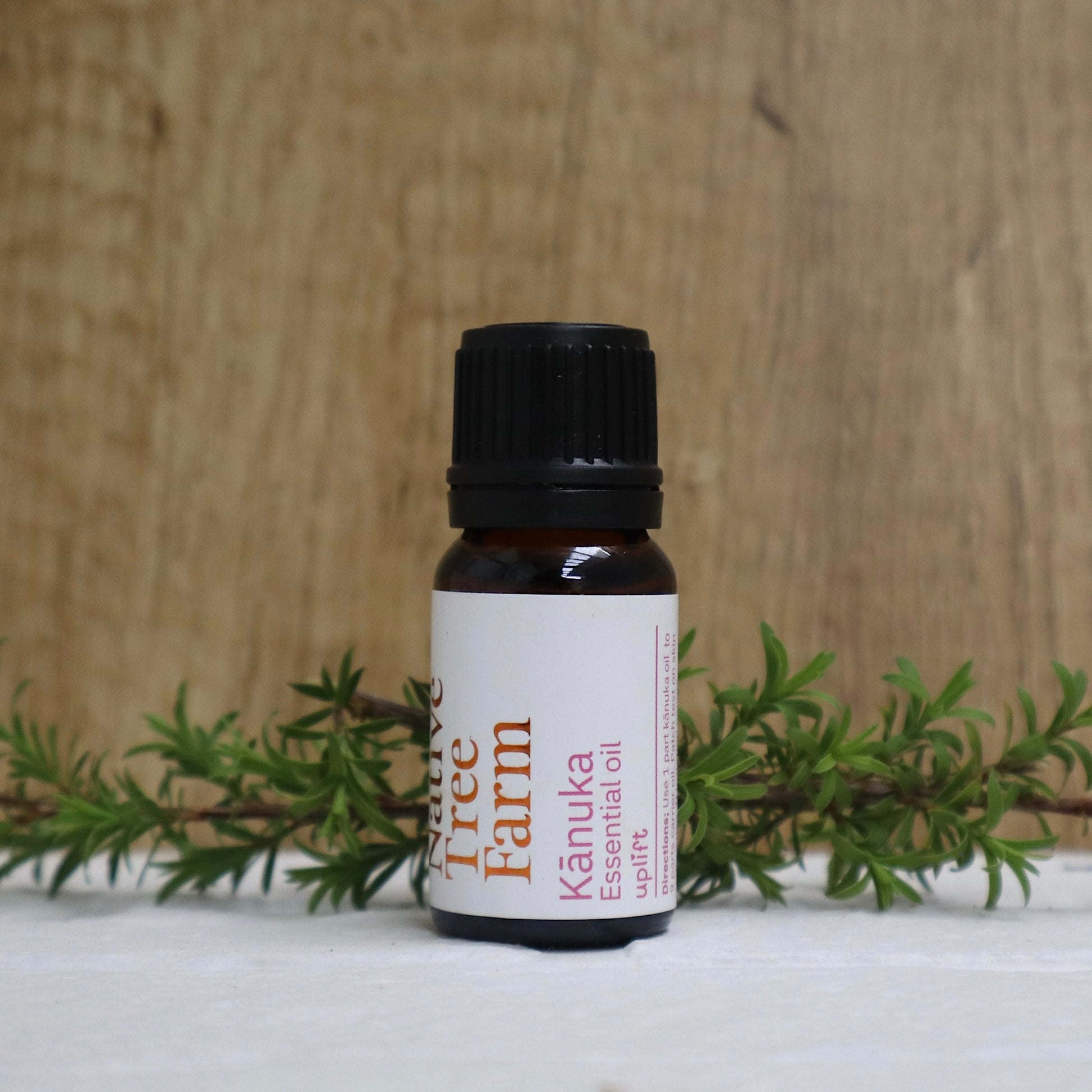 Bottle of Kānuka essential oil from Native tree Farm with green leaves on a wooden background