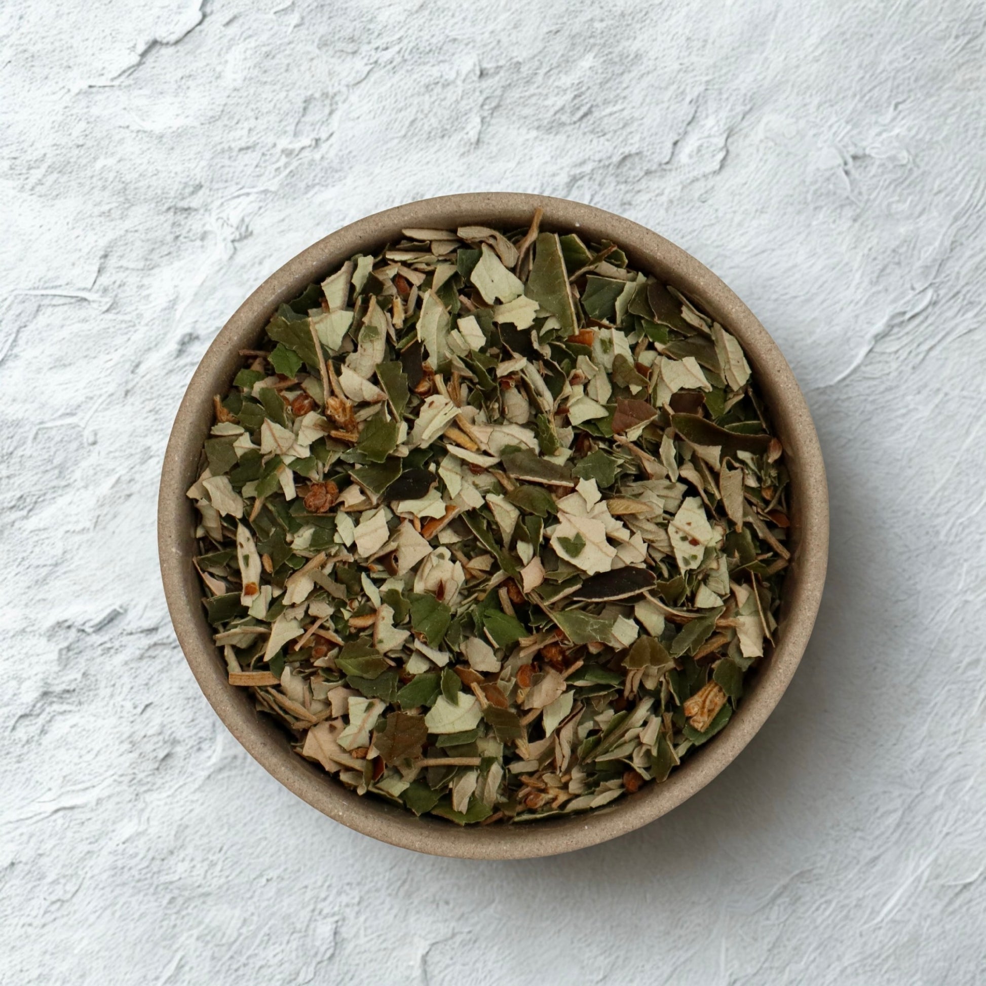 Bowl of dried kumarahou leaf from Native Tree Farm on a light gray stone background