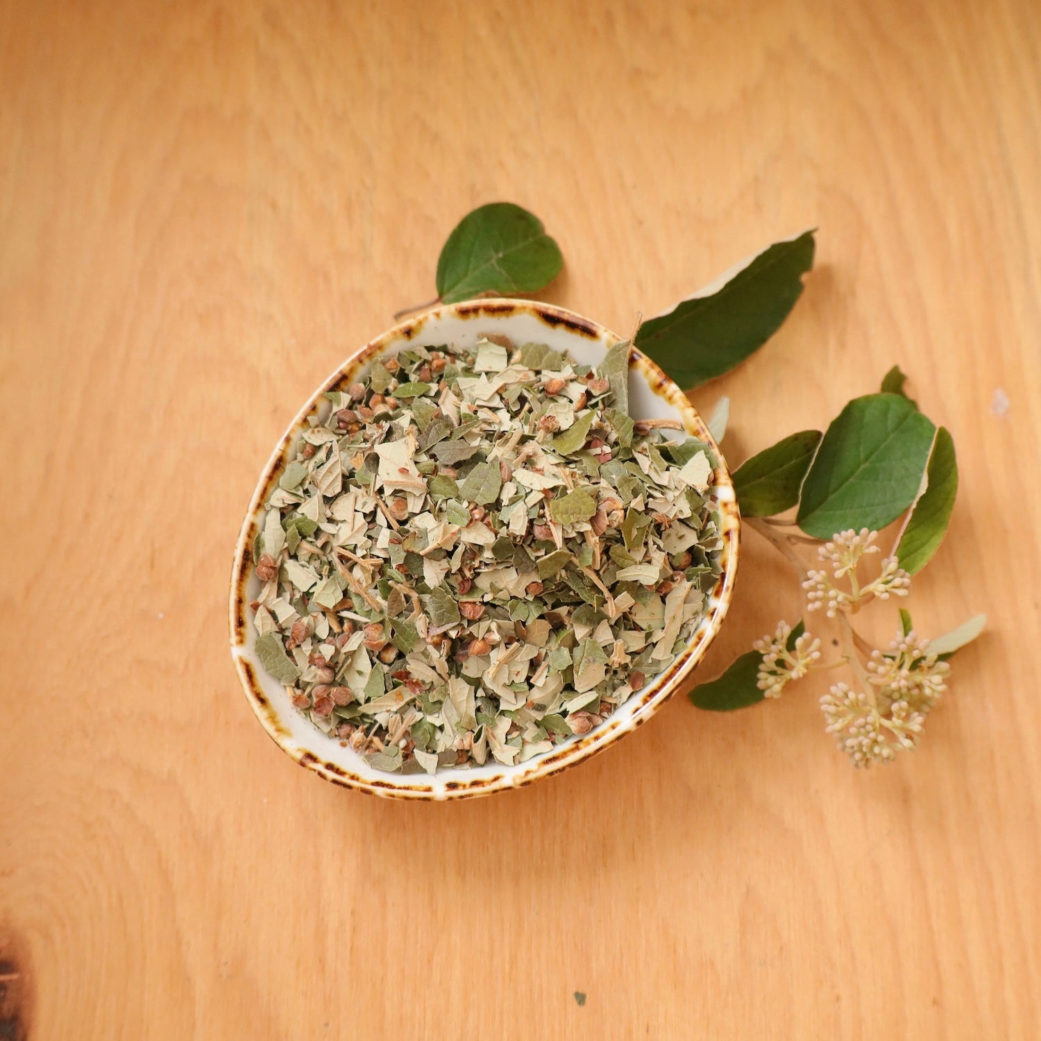 Small bowl filled with dried kumarahou leae on a wooden surface.