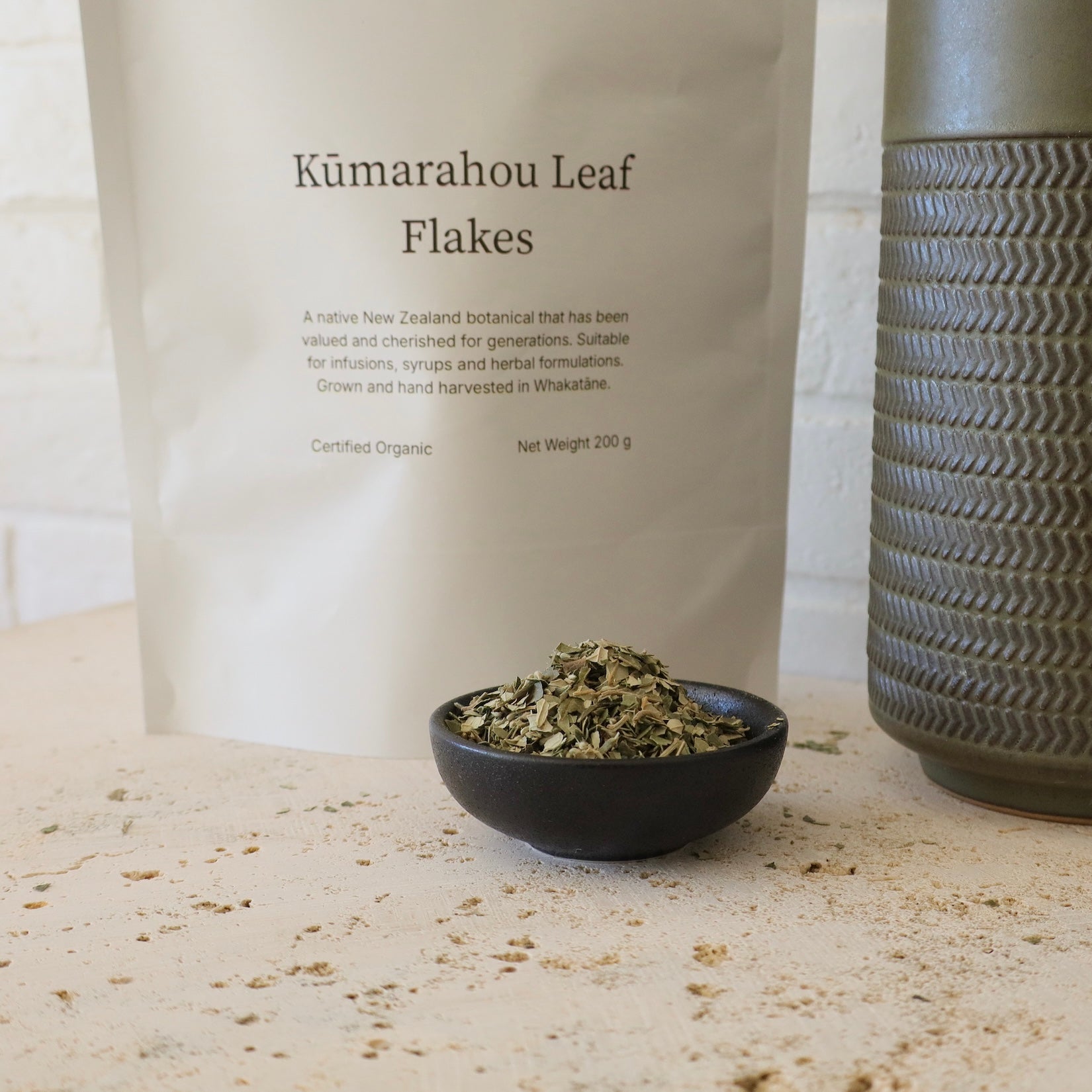 Native Tree Farm kumarahou leaf flakes in small black pottle sitting on the bench