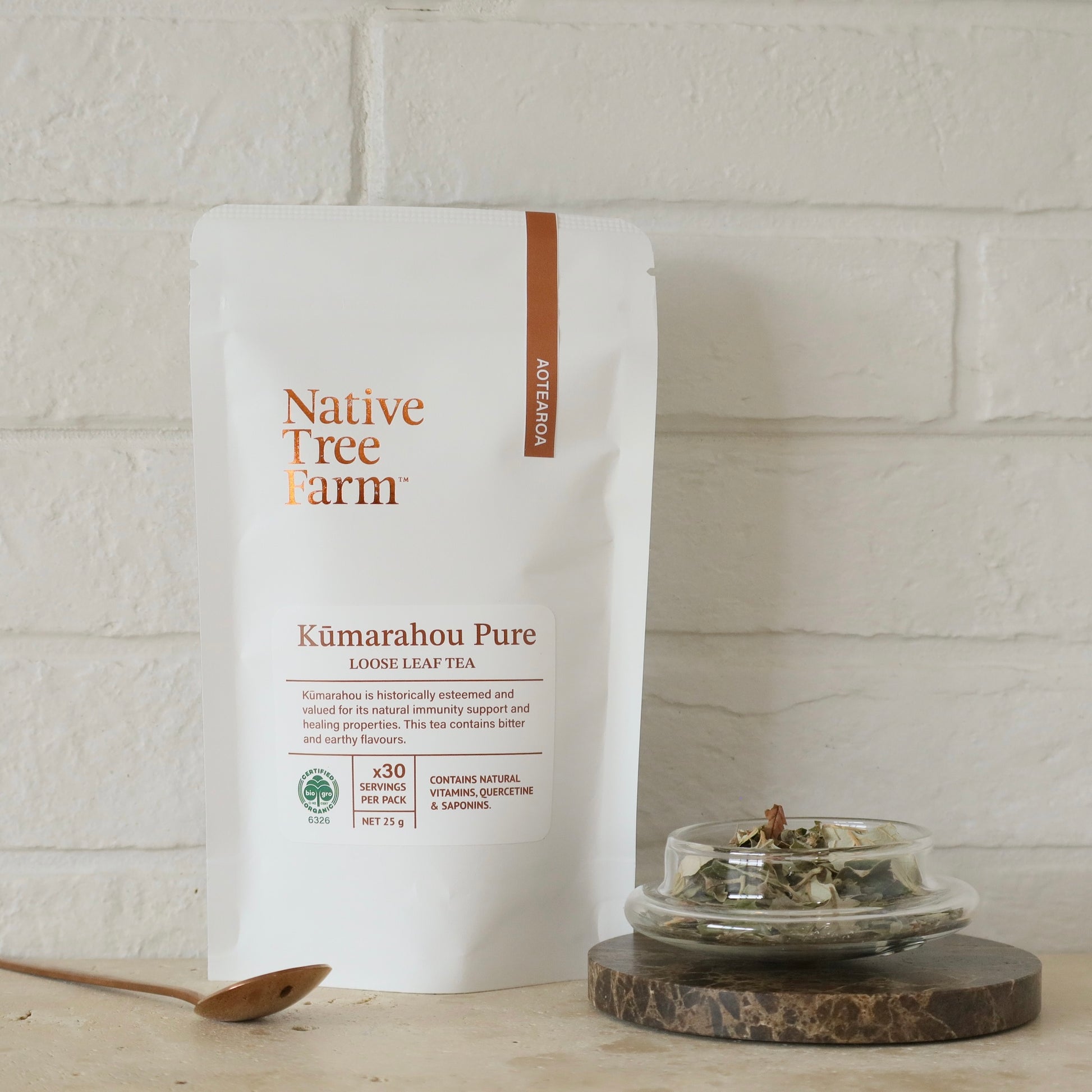 Native Tree Farm Kumarahou Pure loose leaf tea package on a wooden surface with a white brick wall background.