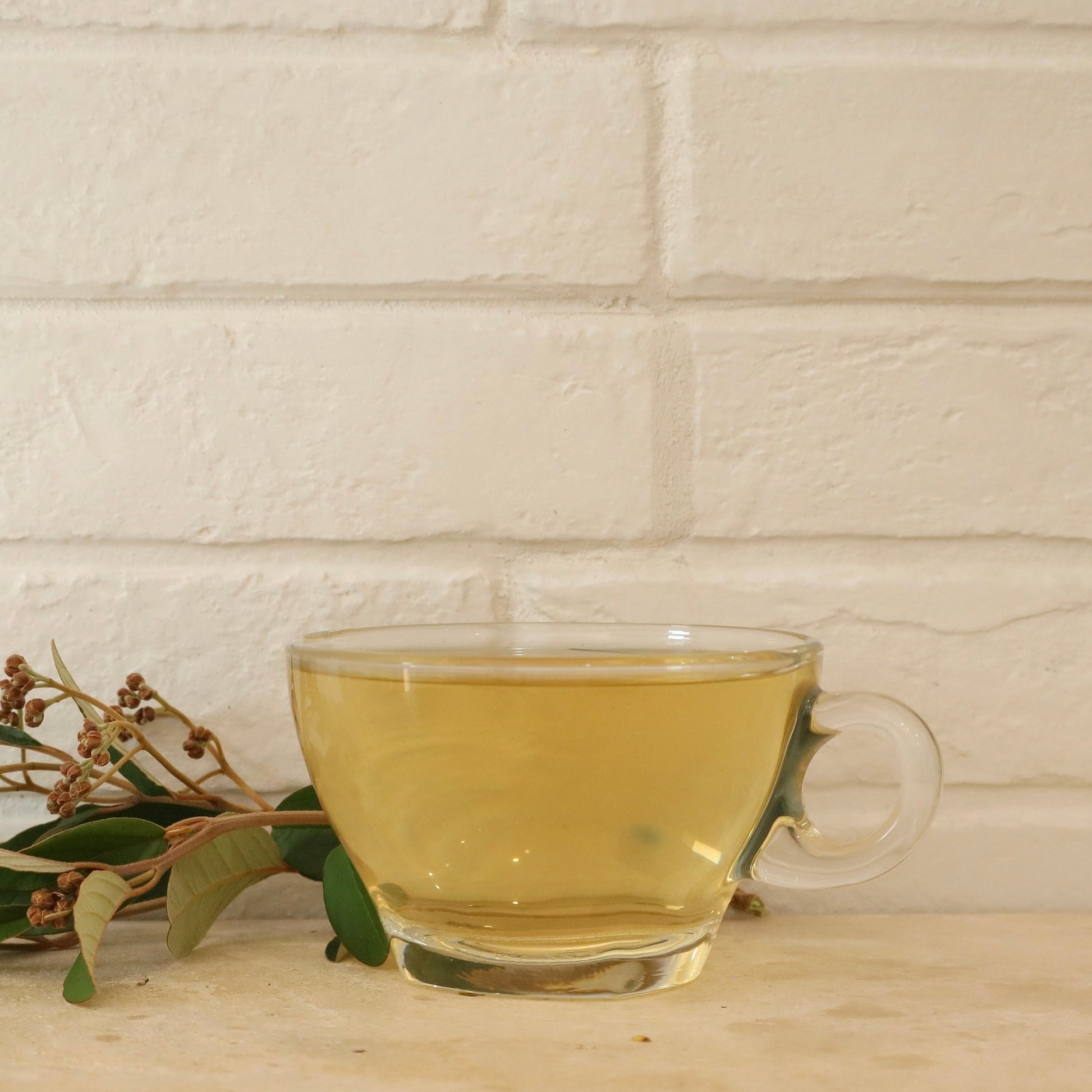 Clear glass mug with kumarahou tea on a wooden surface and light brick wall background