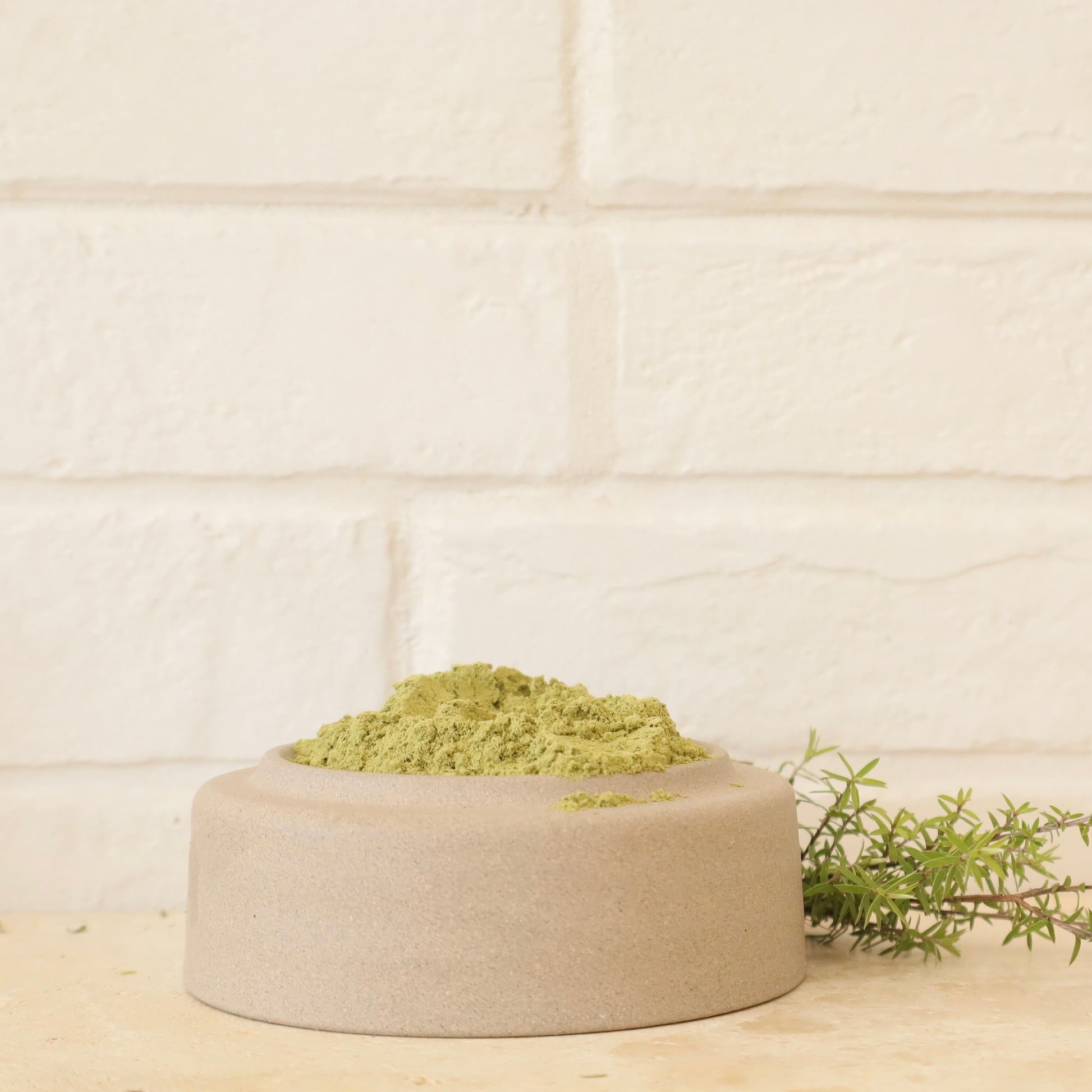 Green manuka leaf powder from Native Tree Farm - in a beige container on a light wooden surface with a tiled wall background