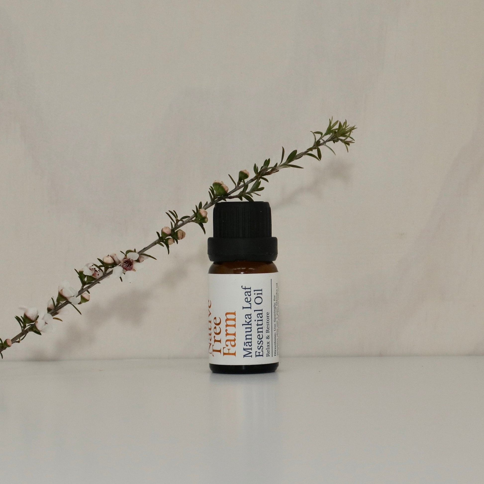 Bottle of Native Tree Farm Manuka Leaf Essential Oil with a manuka branch on a neutral background