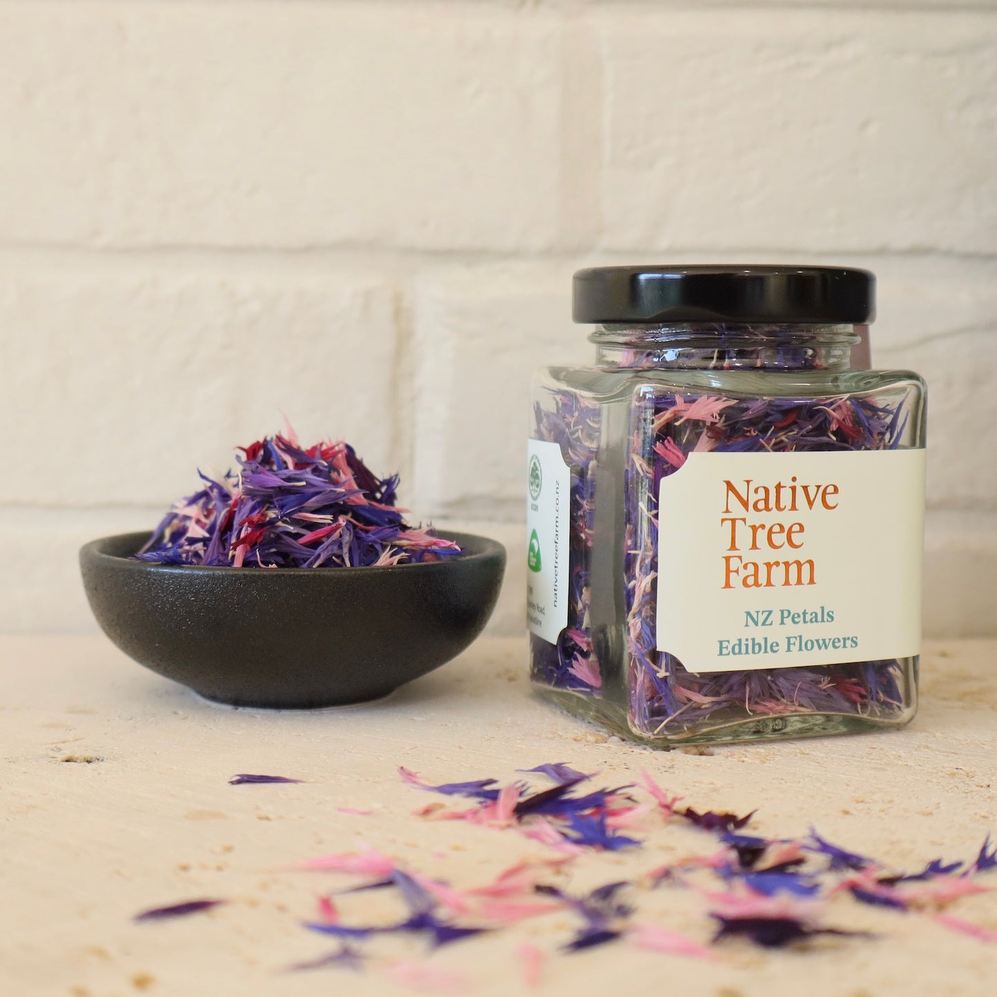 A glass jar of Native Tree Farm Petals Edible Flowers in it on a travertine stone bench.