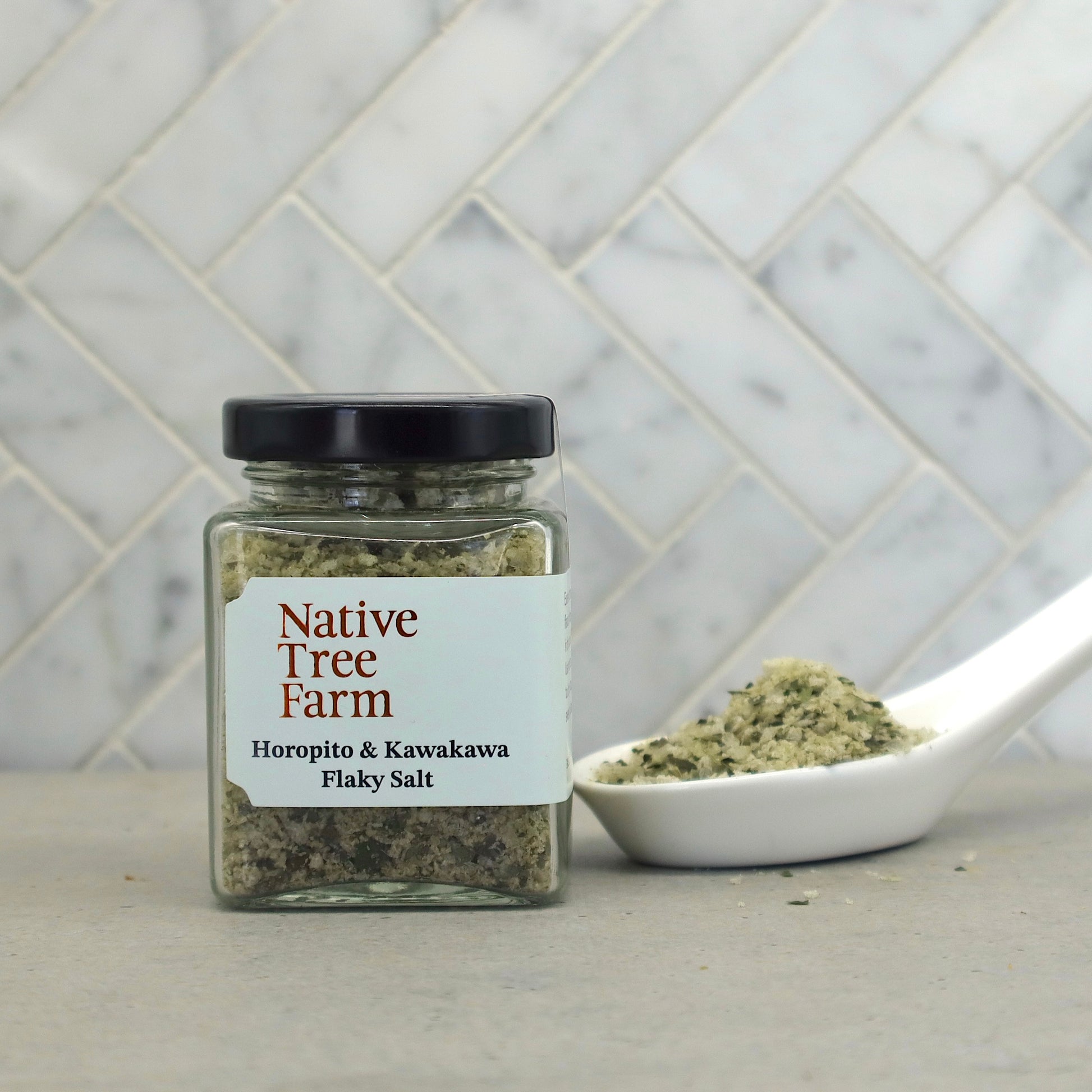 Jar of Native Tree Farm Horopito & Kawakawa Flaky Salt with a spoonful of flaky salt on a stone table