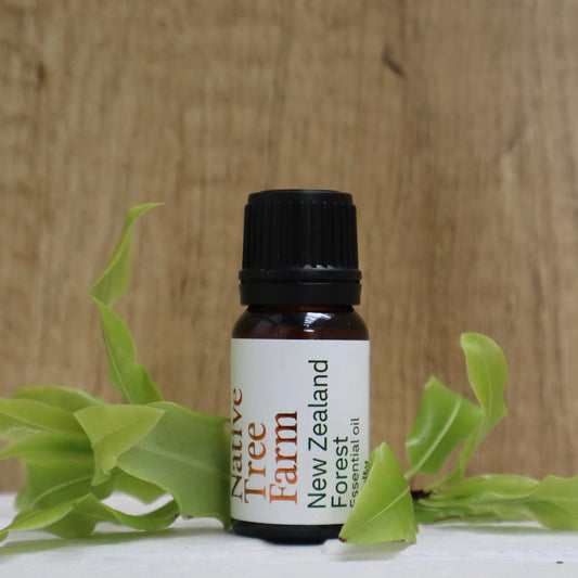 Bottle of New Zealand Forest essential oil from Native Tree Farm with green leaves on a wooden background
