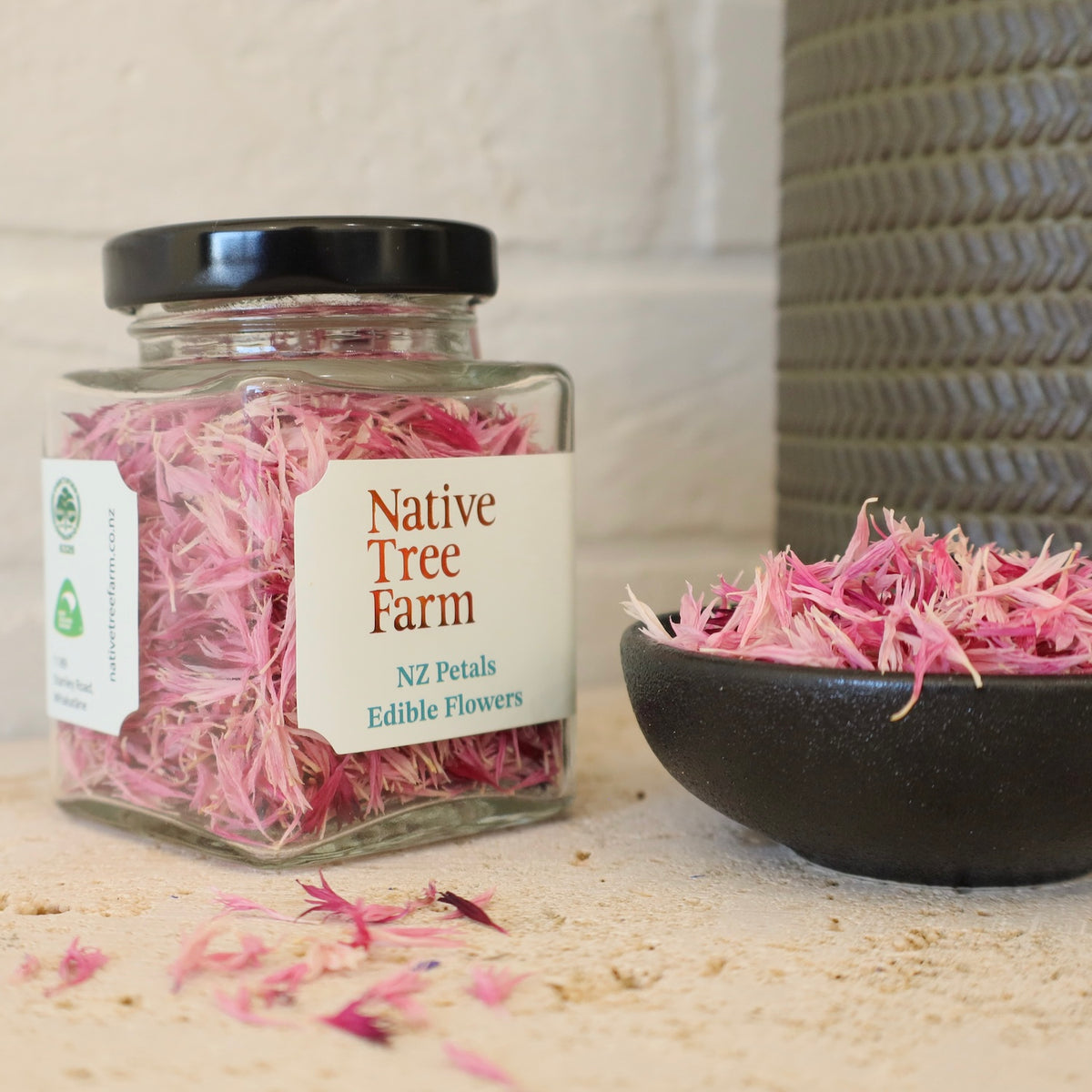 a jar of Native Tee Farm pink edible flower petals on the a travertine bench