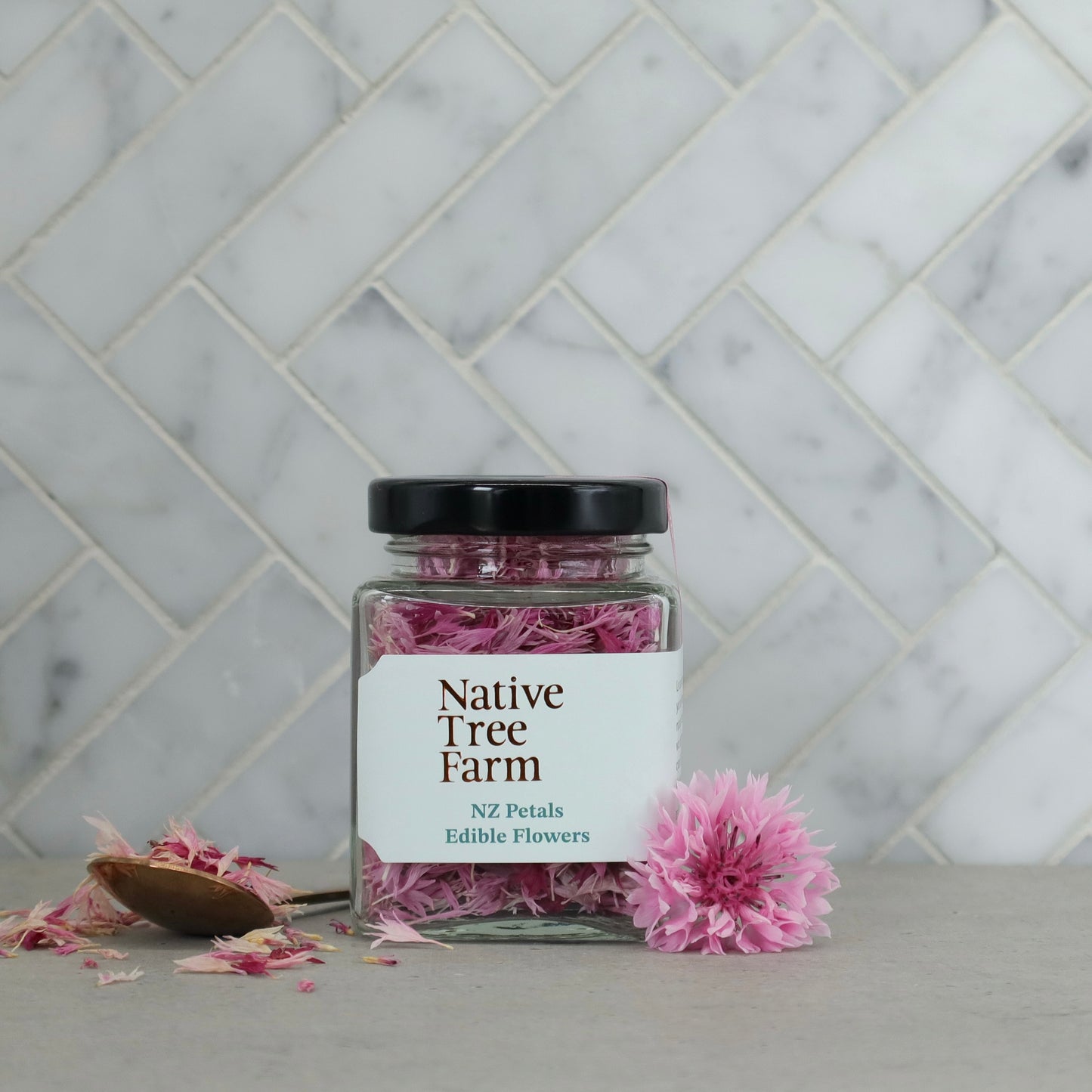 Jar of pink flowers from Native Tree Farm on a marble surface with a tiled wall background