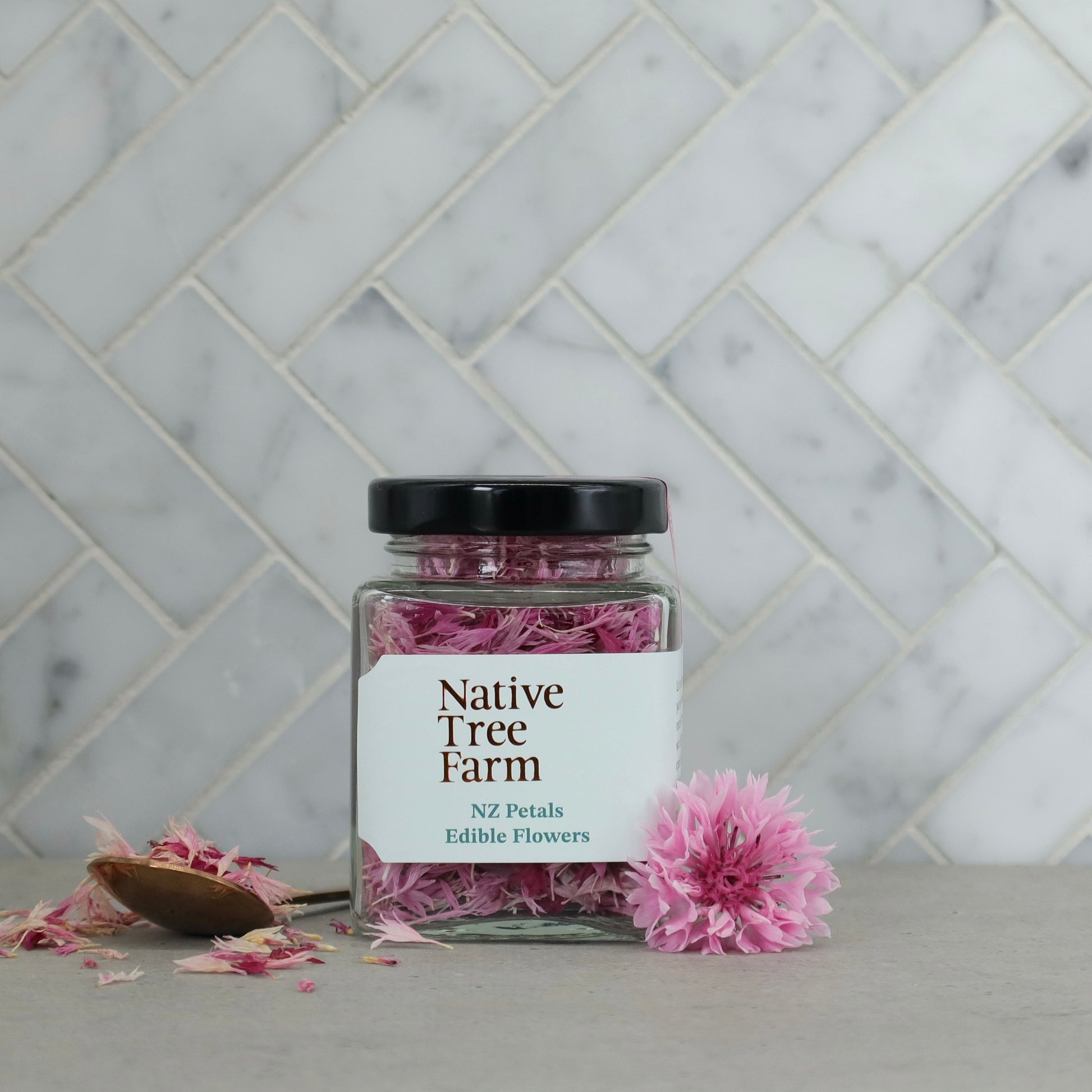 Jar of pink flowers from Native Tree Farm on a marble surface with a tiled wall background